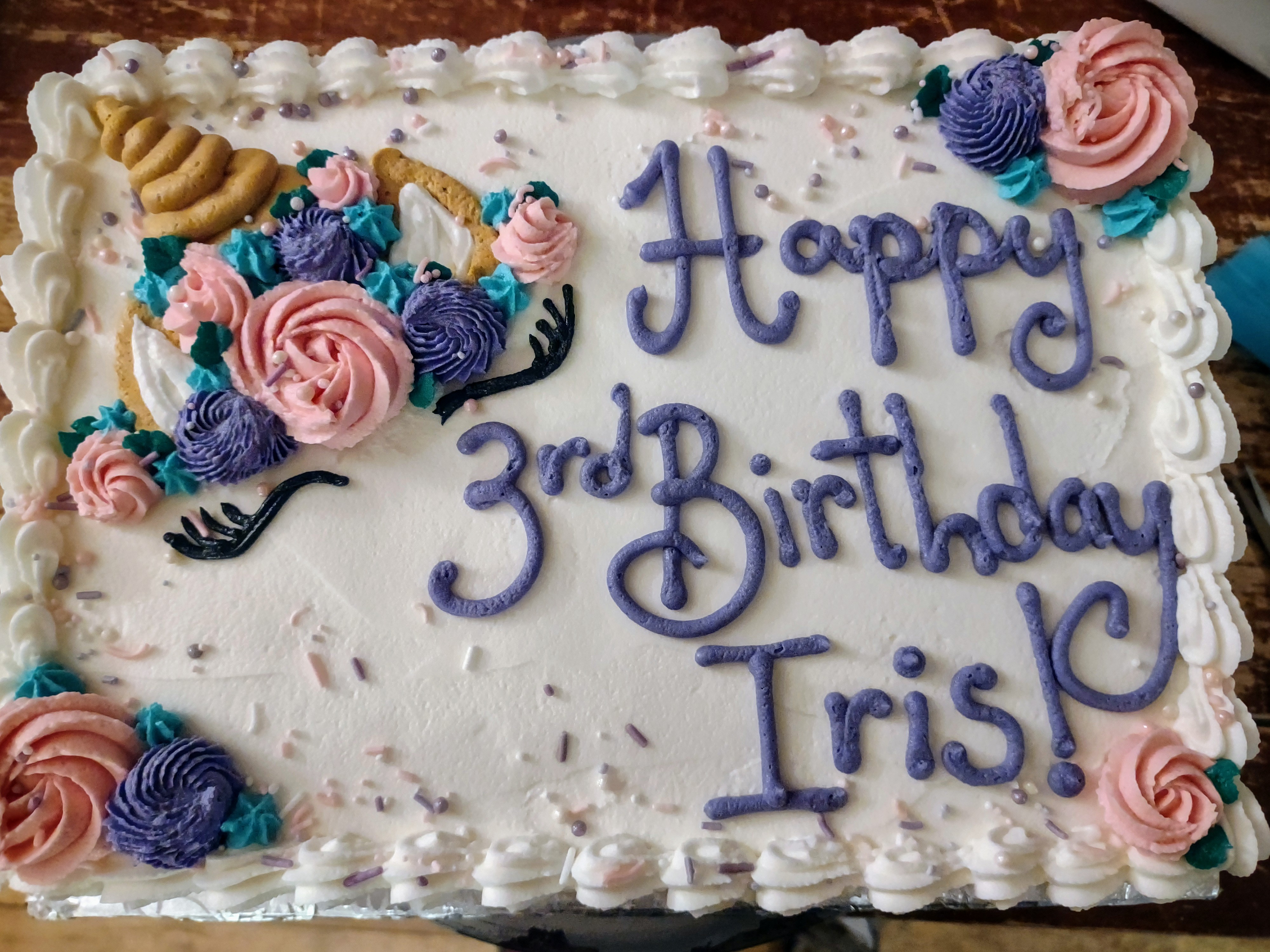 A decorated birthday cake featuring pastel flowers and the message 'Happy 3rd Birthday Iris!' in colorful icing.